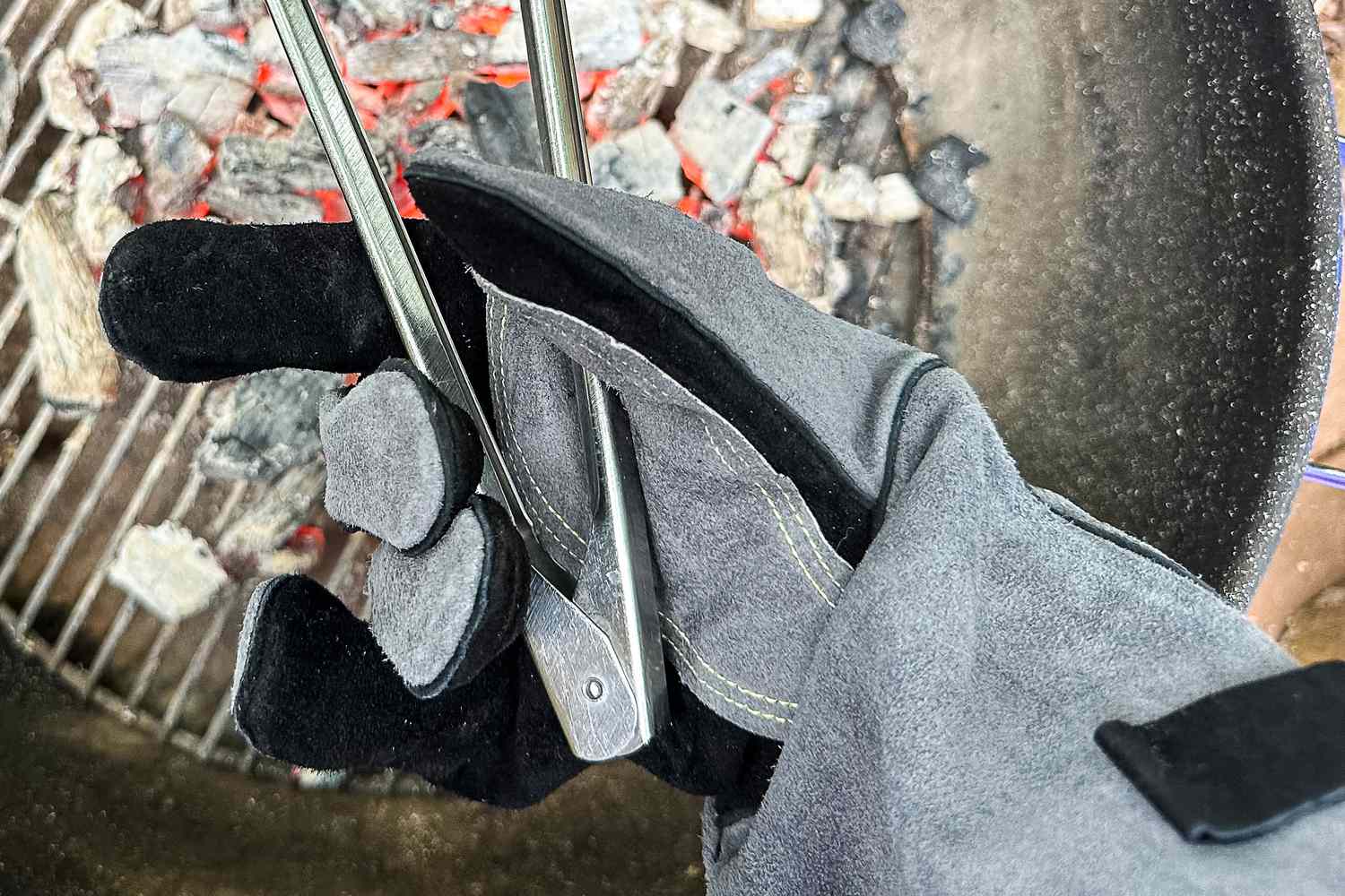 A person holds a pair of tongs while wearing the Breeo Fire Pit Gloves
