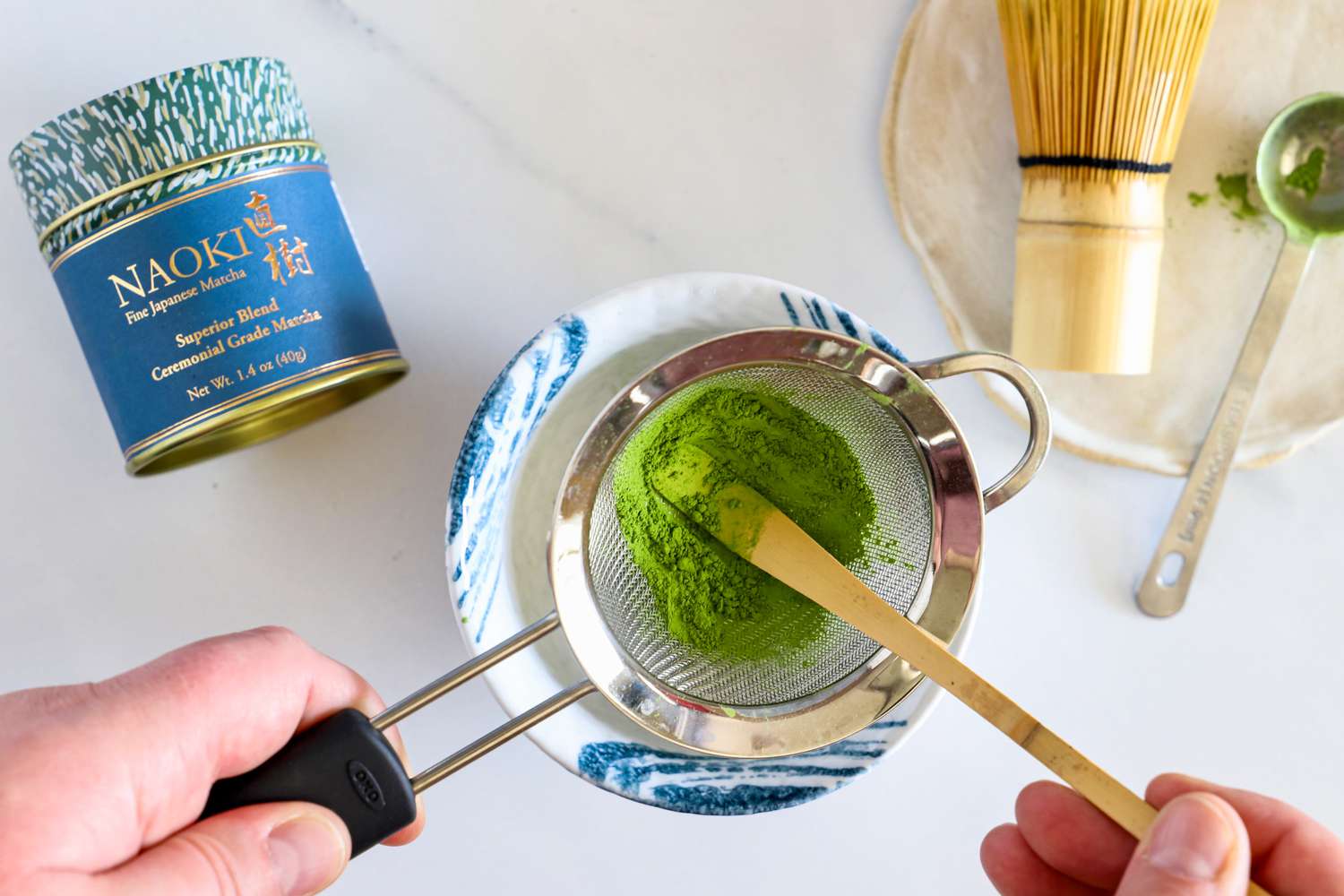 A person sifting Naoki Matcha Superior Ceremonial Blend into a cup, next to the container
