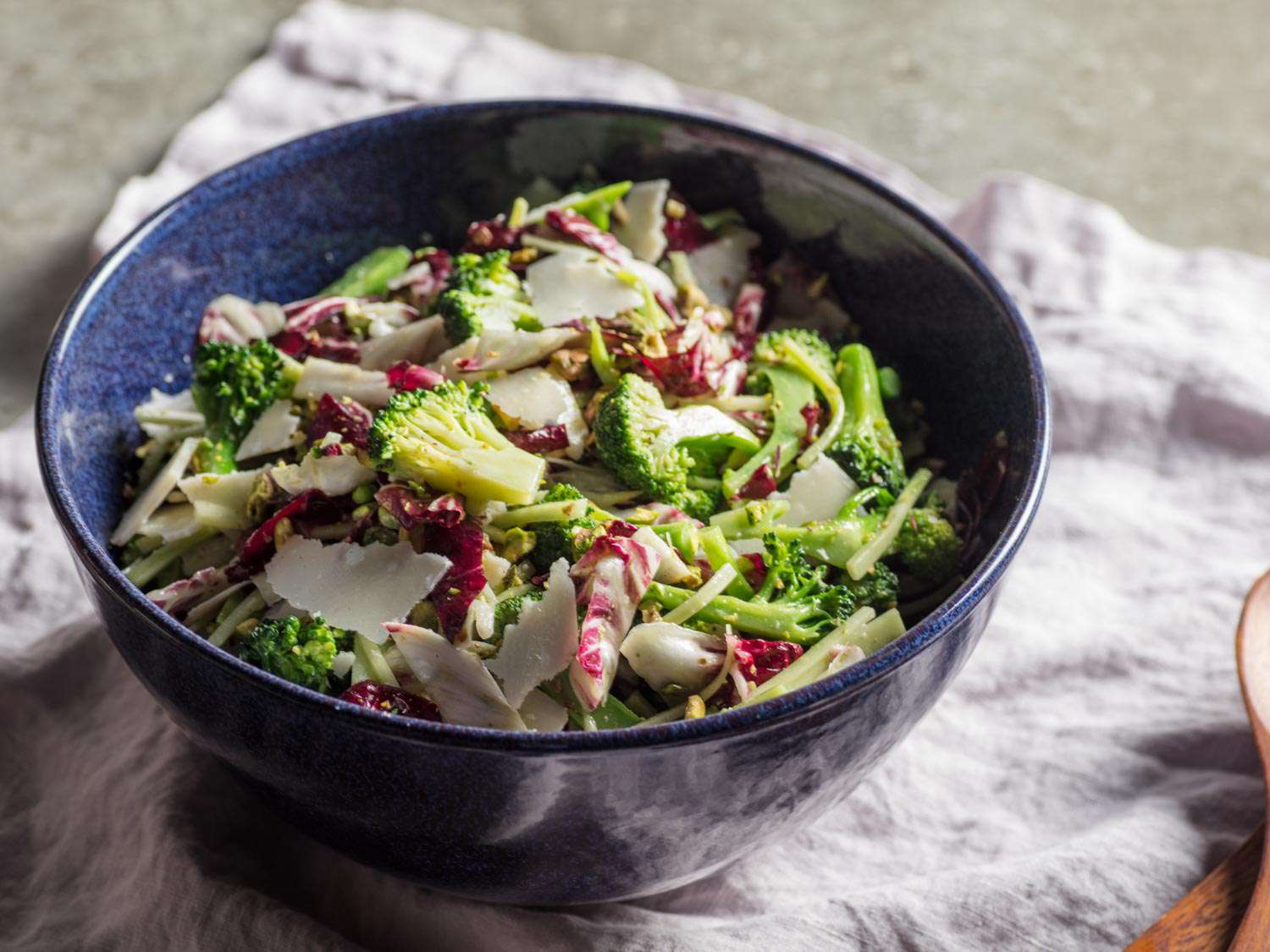 Broccoli salad with radicchio, basil, and pistachios in a blue bowl.