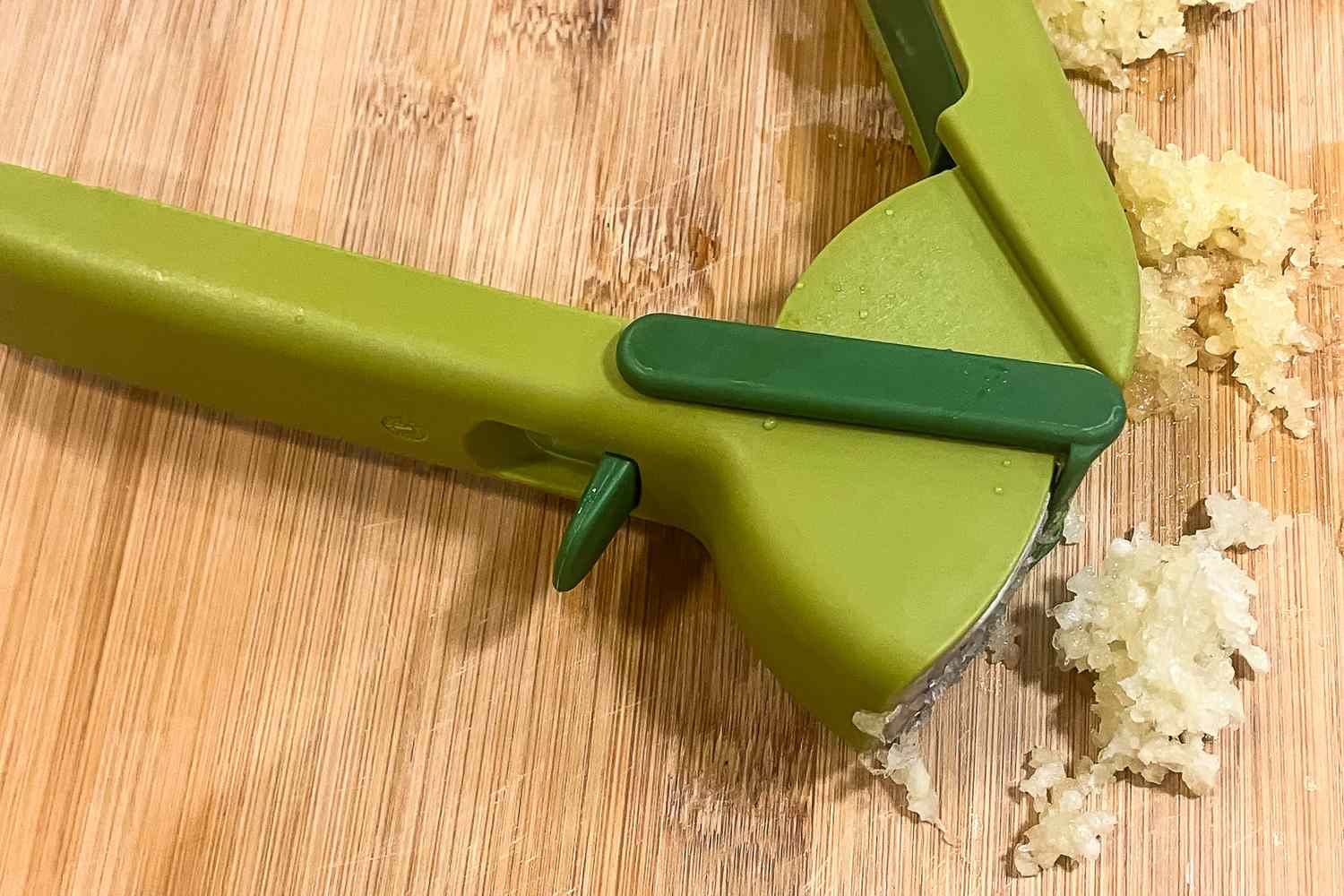 A hand garlic press on a wooden surface with pressed garlic surrounding it