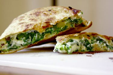 Side view of a spinach pie quesadilla, sliced into wedges and arranged on a cutting board.