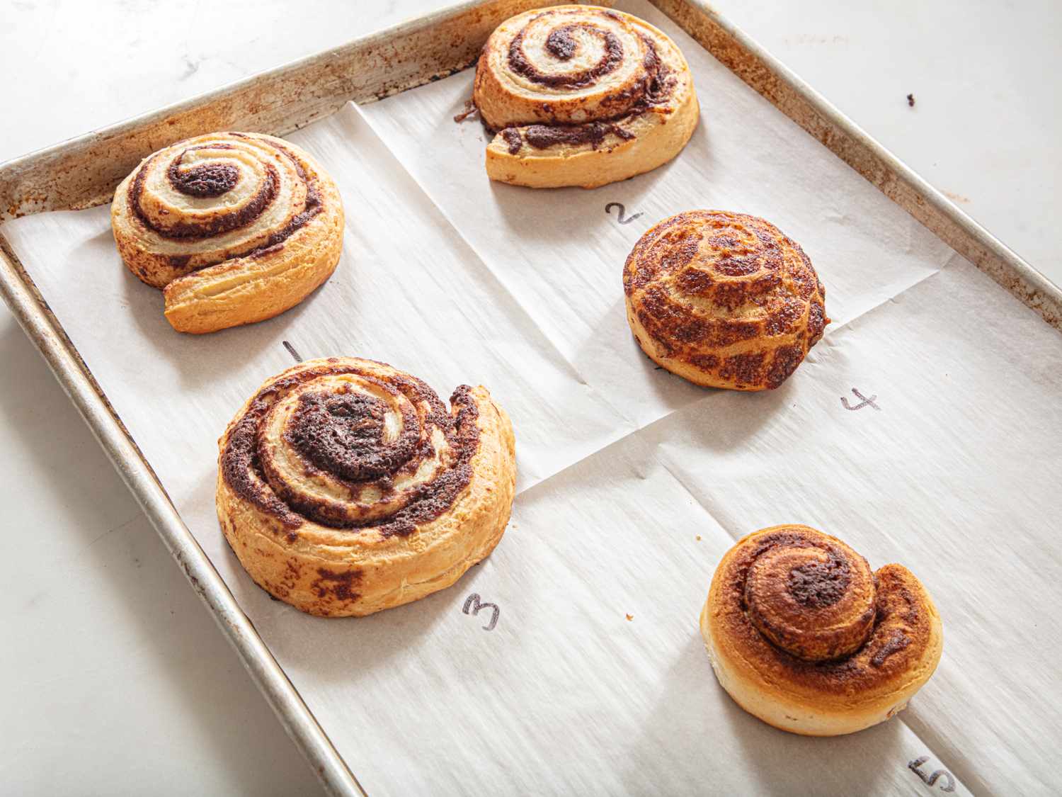 A tray with four cinnamon rolls labeled 1 to 4 on parchment paper