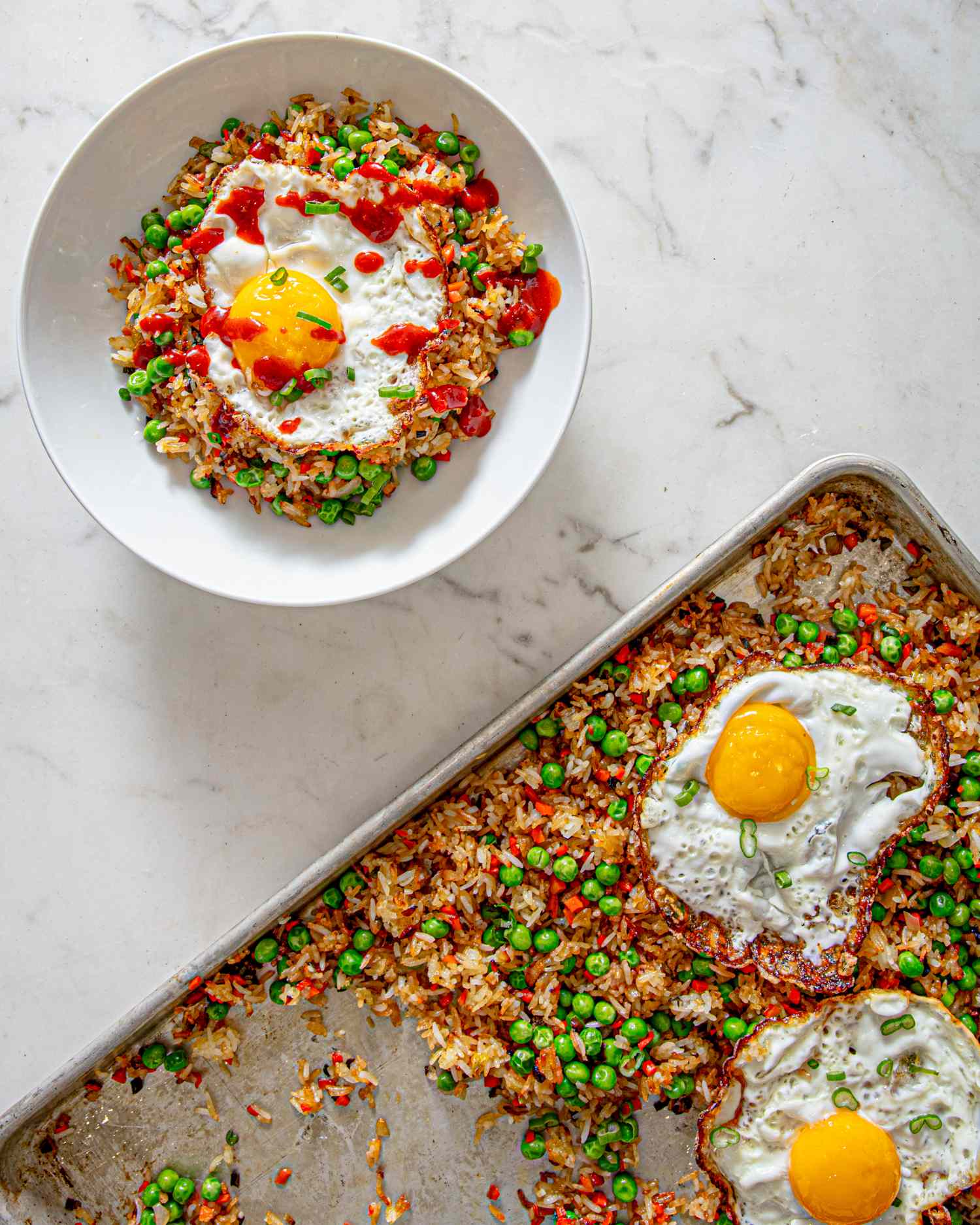 Sheet pan fried rice served with eggs, peas, and seasoning, shown on a baking sheet and a serving bowl