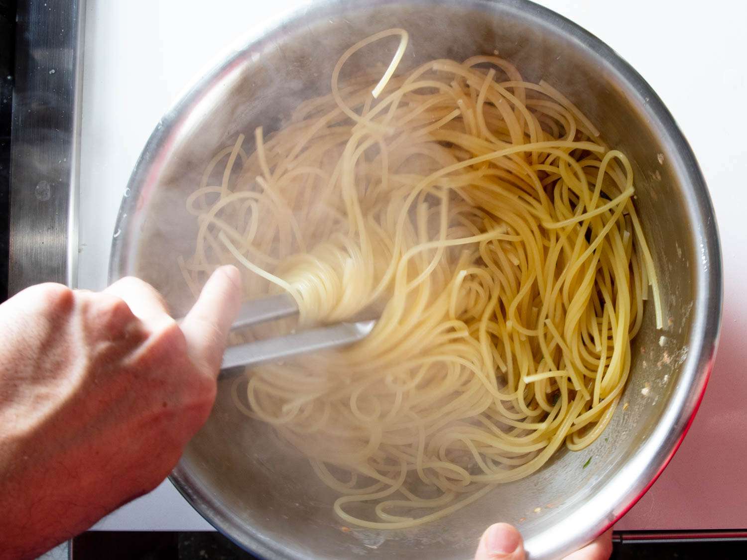 A hand twirling spaghetti with tweezers. 