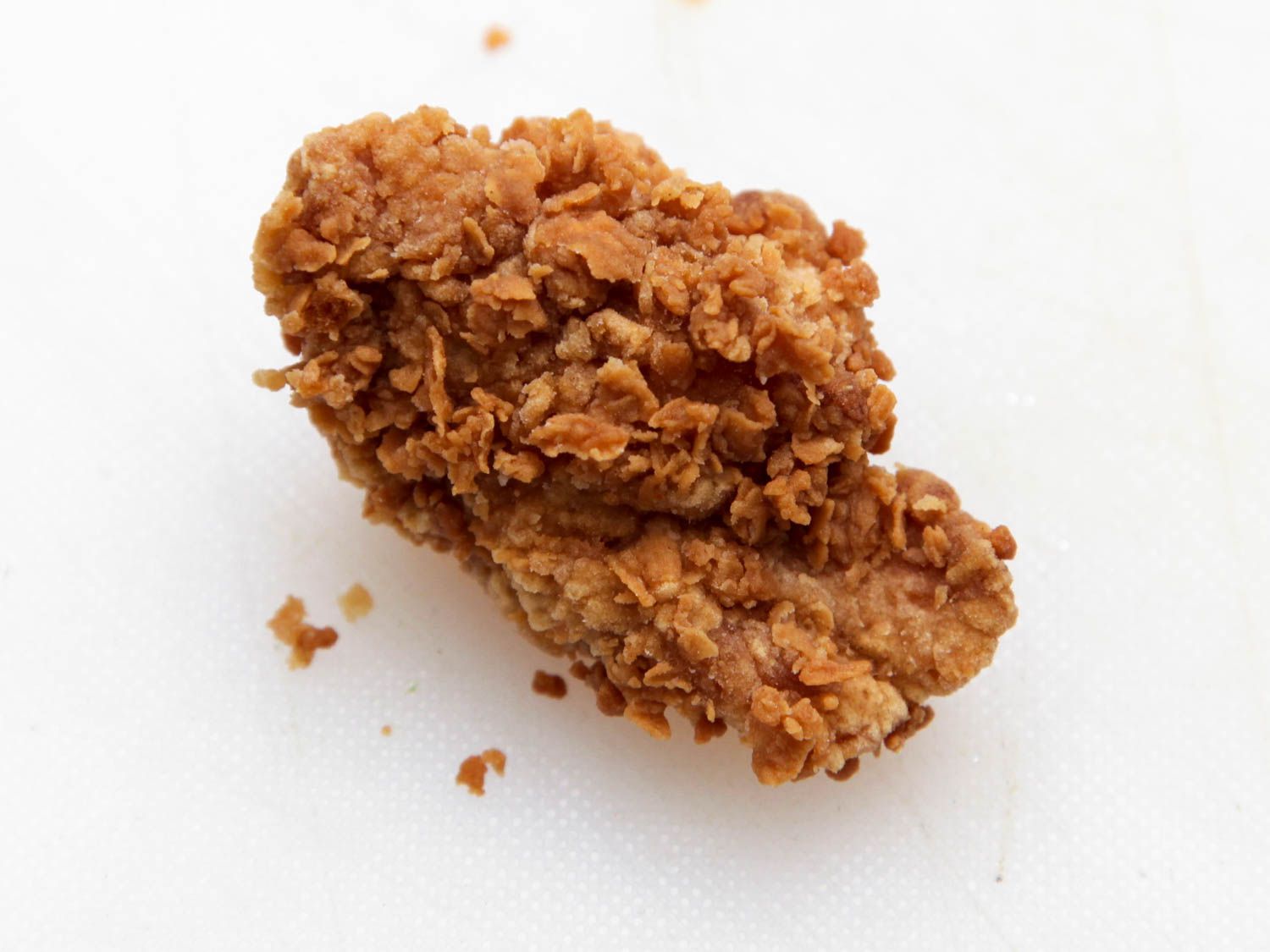 A piece of fried chicken resting on a white surface. 
