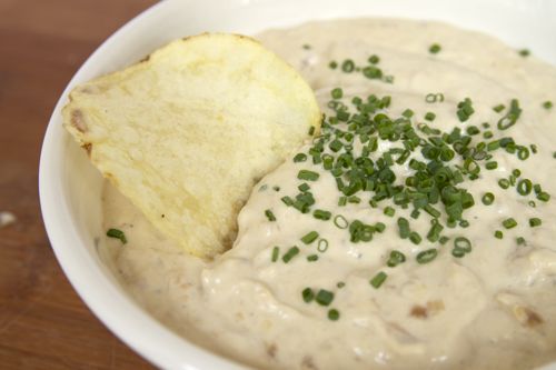A close-up shot of a bowl of French onion dip with a potato chip in it.