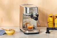 Espresso coffee brewing into glass mug from Breville Bambino Plus Espresso Machine on white marble countertop