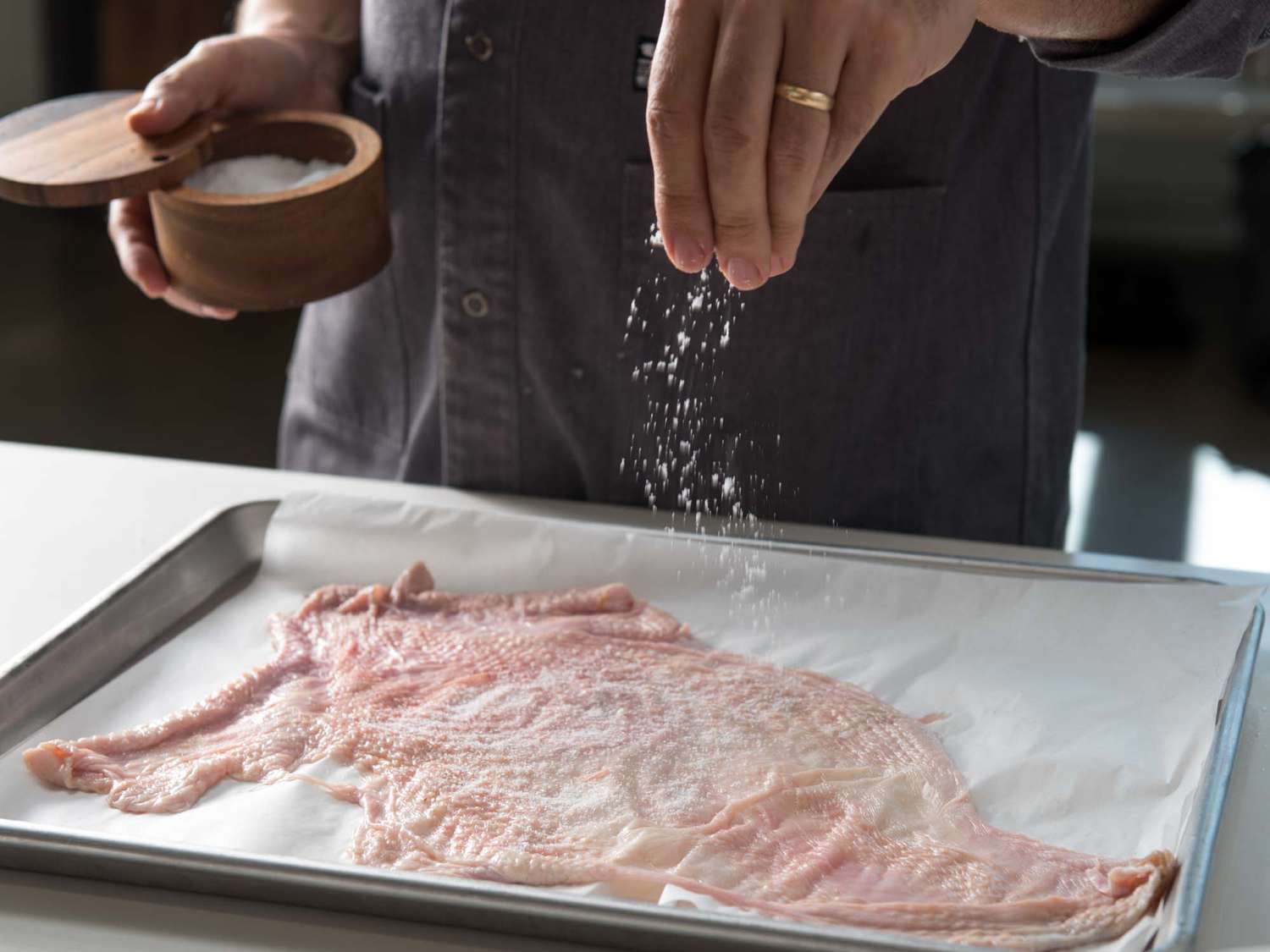 Seasoning turkey skin with salt and pepper on a parchment lined baking sheet.