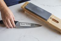 A person reaching for a knife next to a whetstone sharpener