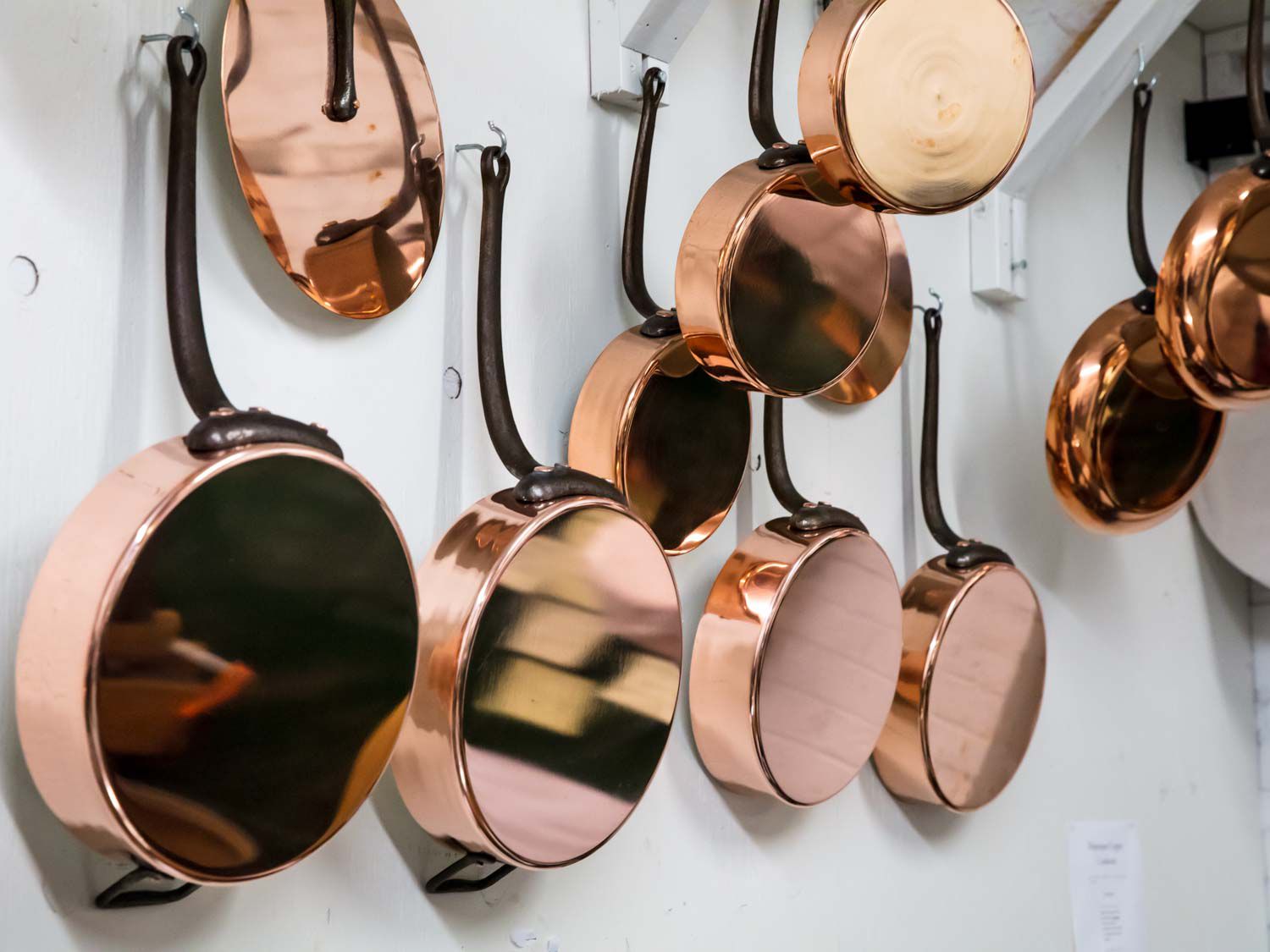 Copper pans hanging from hooks on white wall