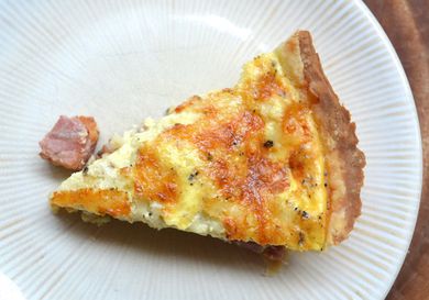 Overhead view of a slice of ham and cheese quiche served on a white plate.