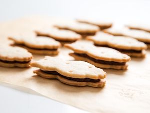 Two rows of fudge-filled, owl-shaped shortbread sandwich cookies on parchment paper.