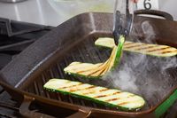 A person uses tongs to flip zucchinis being grilled using the Smithey Ironware Co. No. 12 Grill Pan.