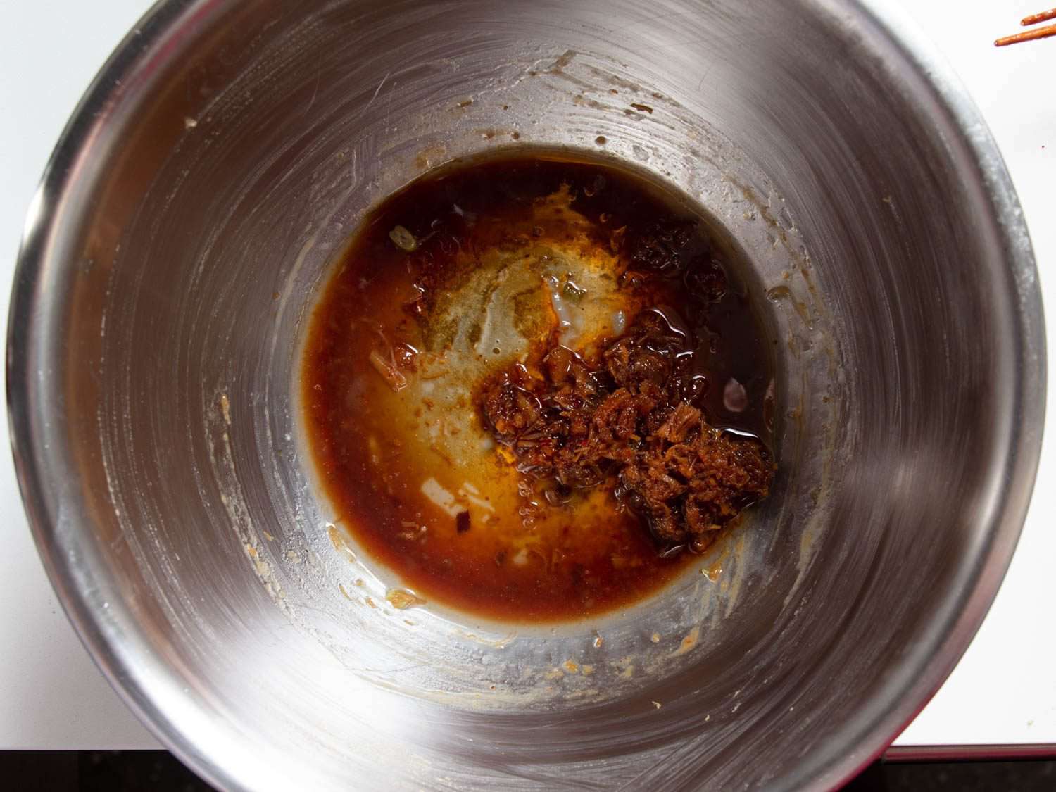 Overhead view of a mixing bowl with a mixture of soy sauce, pork fat, rice vinegar, and XO sauce in the bottom.