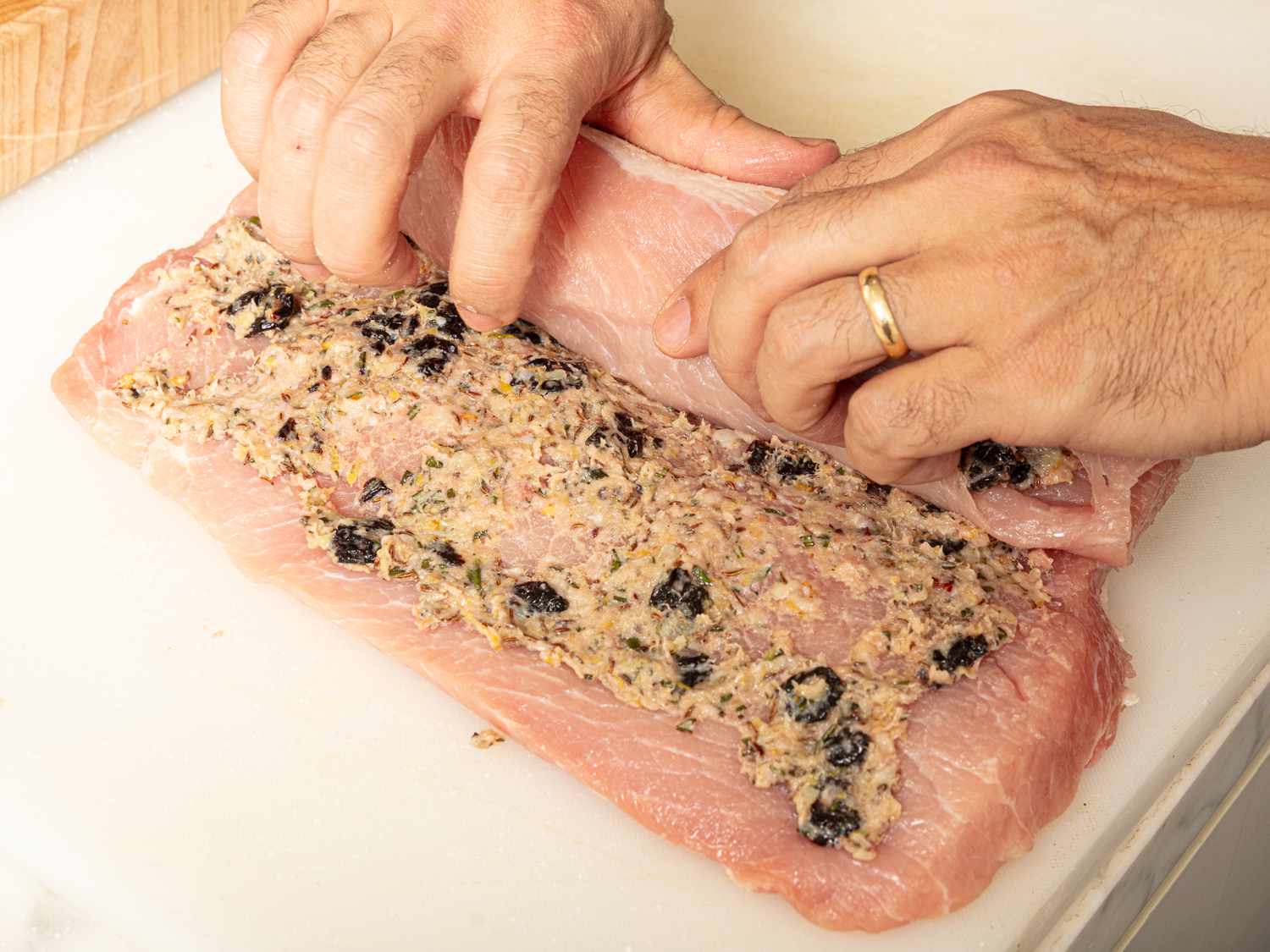 Hands rolling pork loin at tightly into a coil 