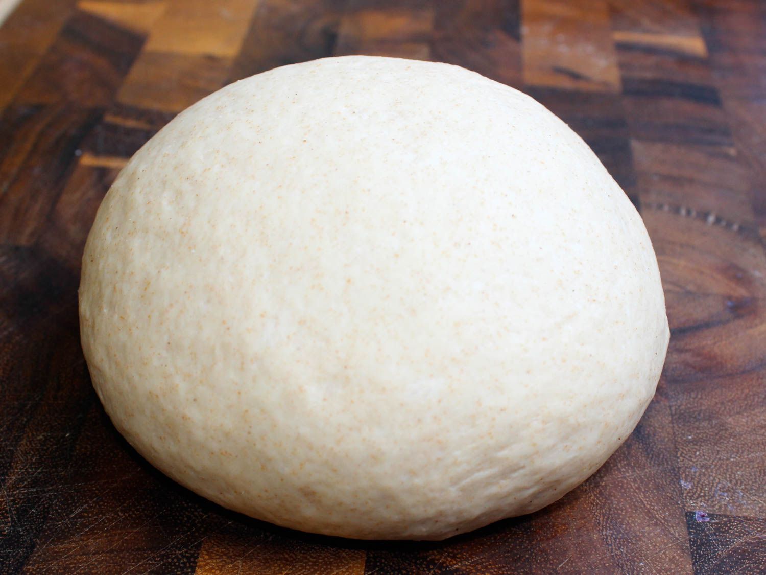 A ball of kneaded pita dough on a wooden surface.