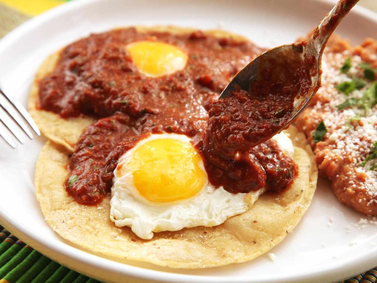 Spooning salsa over fried eggs and tortillas for huevos rancheros.