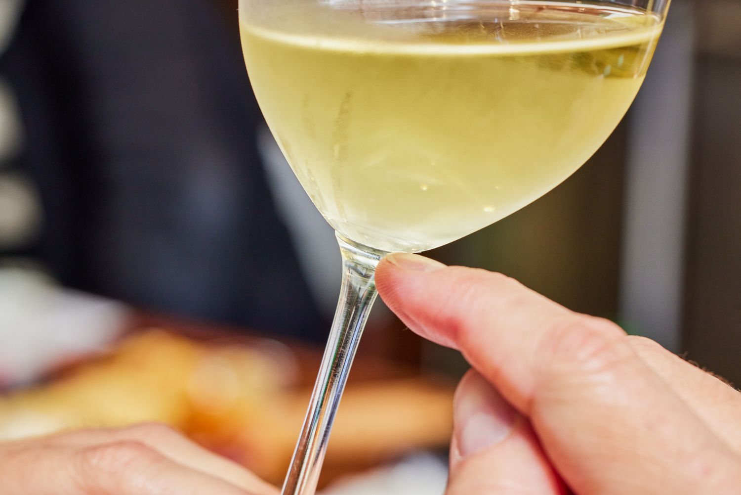 A hand pointing to the stem of a Riedel VINUM Zinfandel/Riesling/Chianti Glass filled with white wine