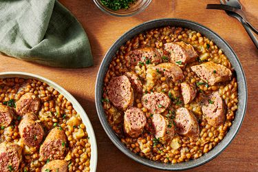 2 bowls of pressure cooked lentils and sausage on a wooden tabletop, with a soft turquoise napkin, two forks, and small bowl of parsley for garnish to the sides. 