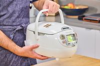 A person lifts the Zojirushi Neuro Fuzzy Rice Cooker and Warmer by the top handle