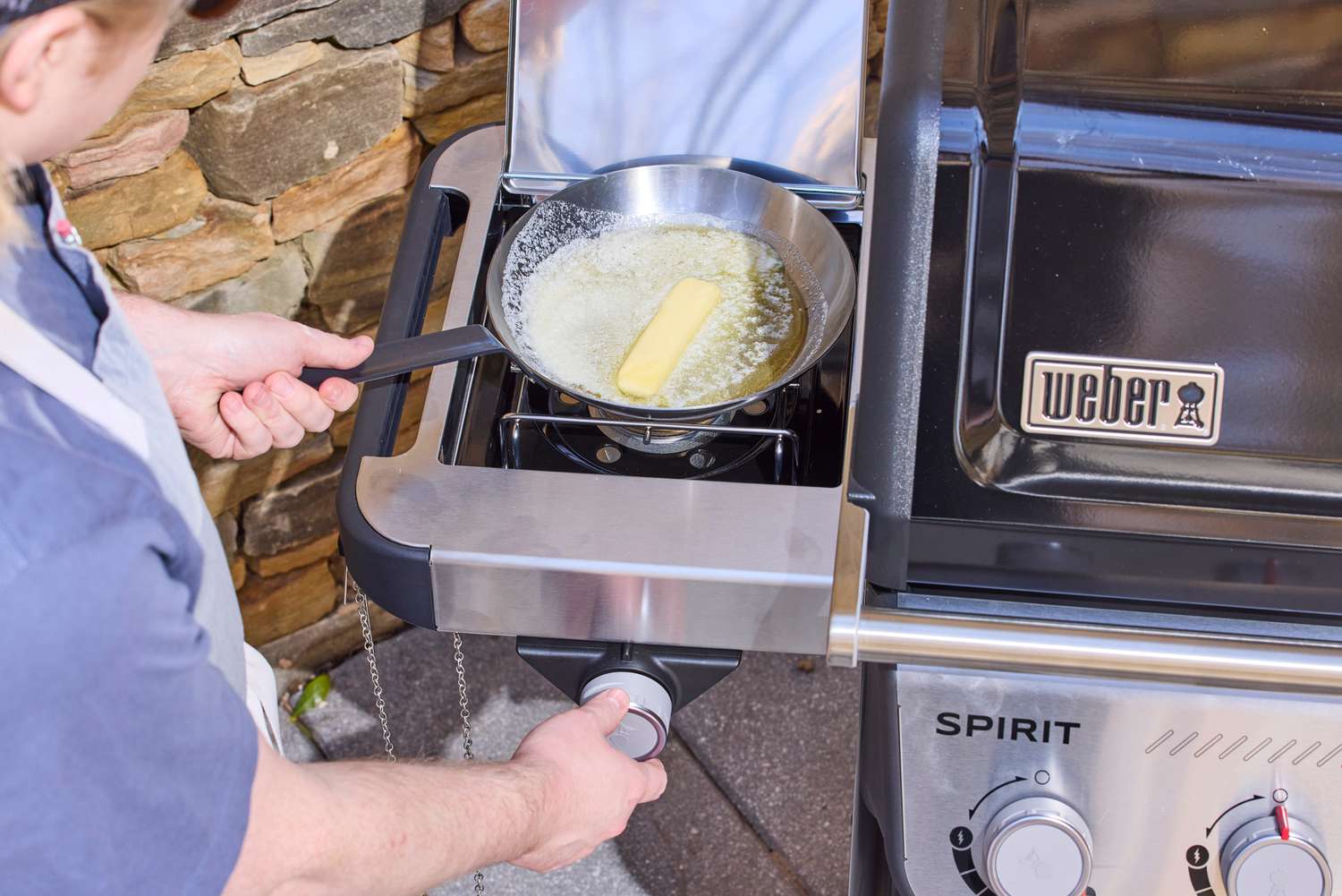 A person melting butter in a pan on the side stove of the Weber Spirit EP-435 Gas Grill