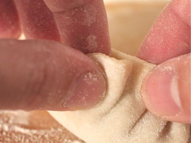 Two hands pleating a handmade dumpling.