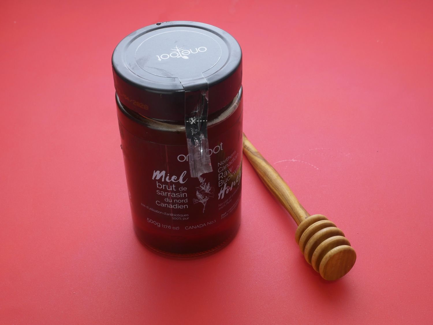 jar of buckwheat honey on red backdrop with honey dripper