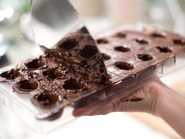 Using a spatula to scrap off excess chocolate from the top of a bonbon mold.