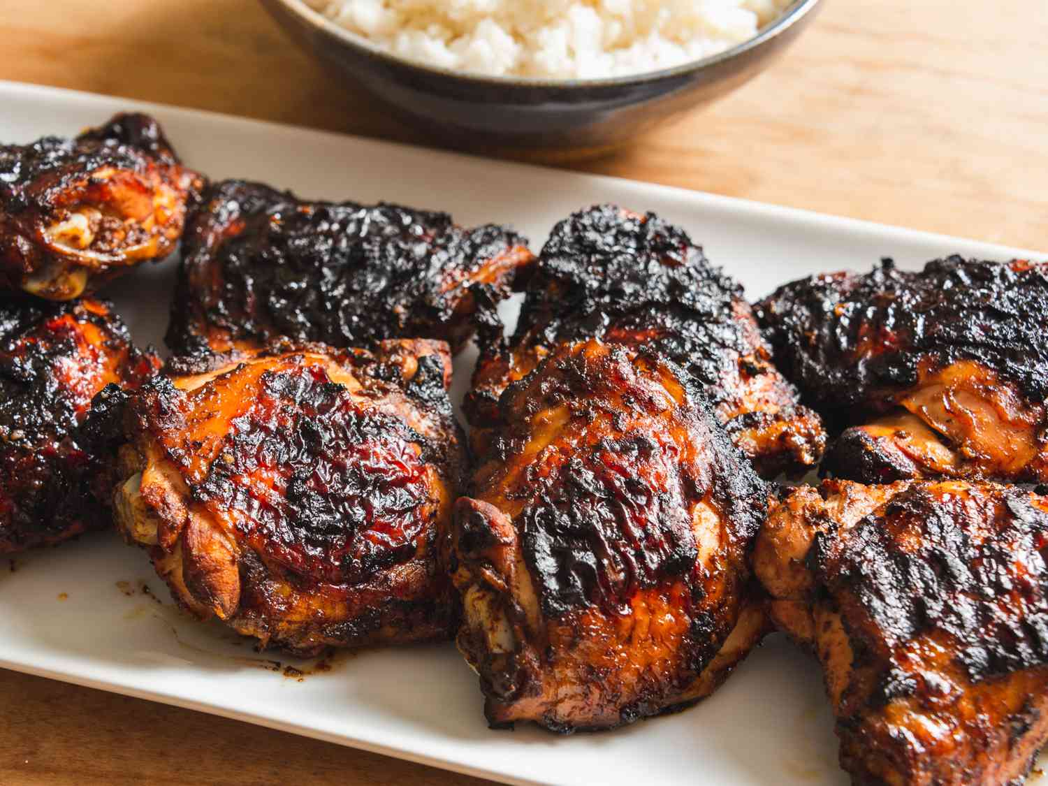 Closeup of the grilled chicken thighs. A bowl of freshly cooked rice is in the background.