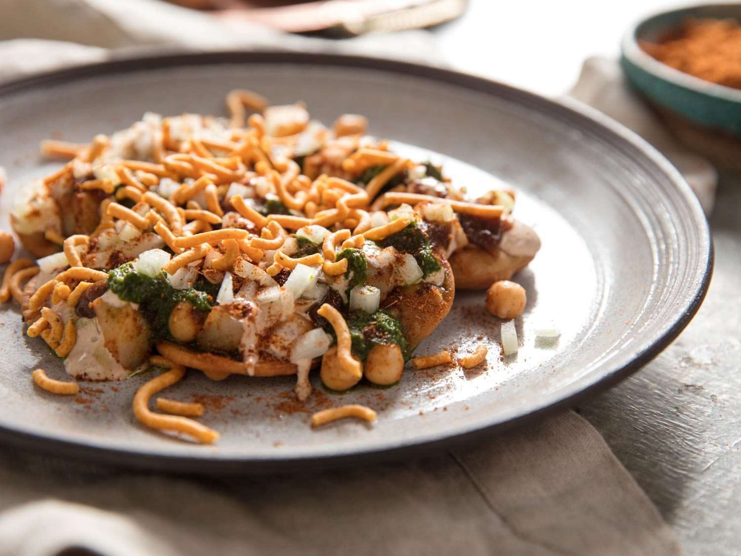A plate of crispy Indian wheat-dough crackers topped with boiled potatoes, chickpeas, yogurt, mint chutney, tamarind chutney, and crunchy fried chickpea noodles.