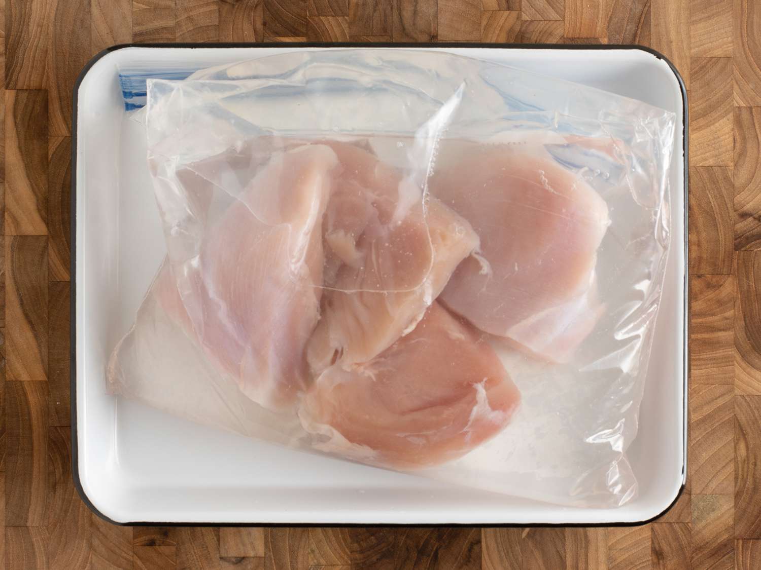 Chicken breasts and brine in a sealed zipper-lock bag, on a white plate.
