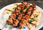 Three skewers of pork souvlaki on a plate with pita bread and tzatziki. 