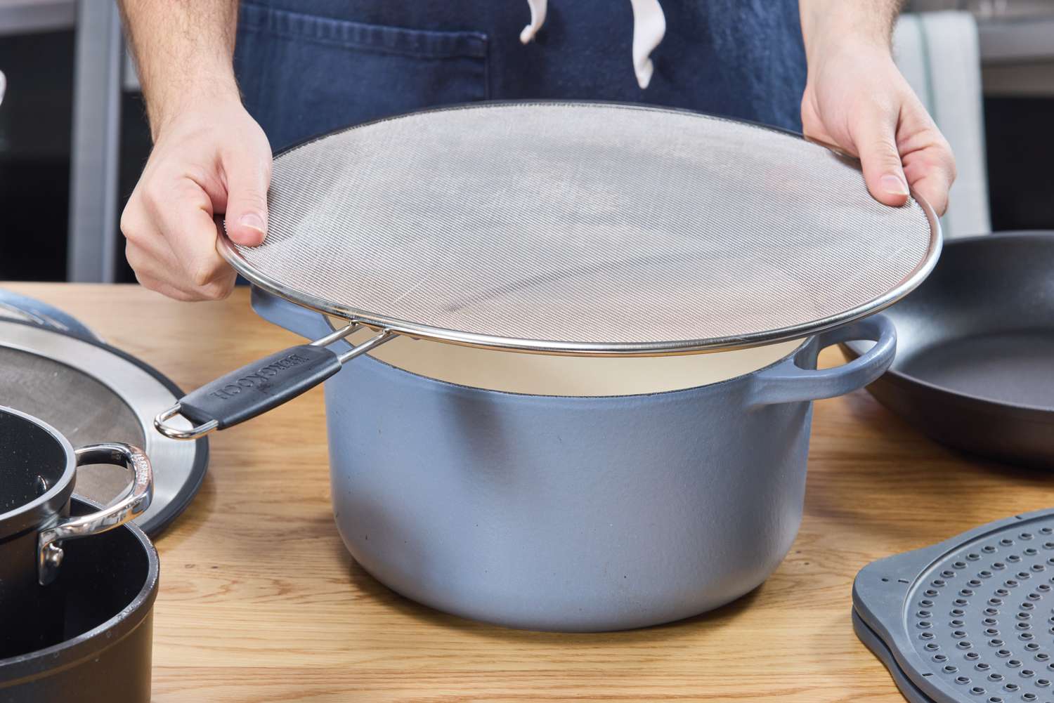a person placing the bergkoch splatter screen over a dutch oven