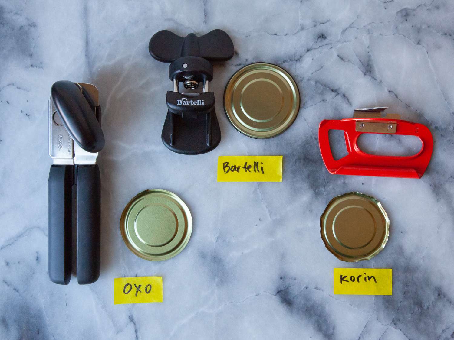 The lids of three cans beside three can openers on marble counter