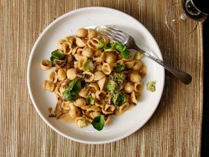 A plate of orecchiette with mushrooms and Brussels sprouts with a glass of wine in the background