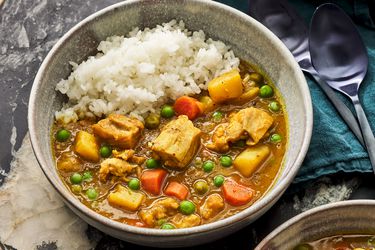 Bowl of KareRaisu with a side of white rice. Curry is in ceramics bowl, and black marble surface, with teal napkin and navy spoons to the right side.
