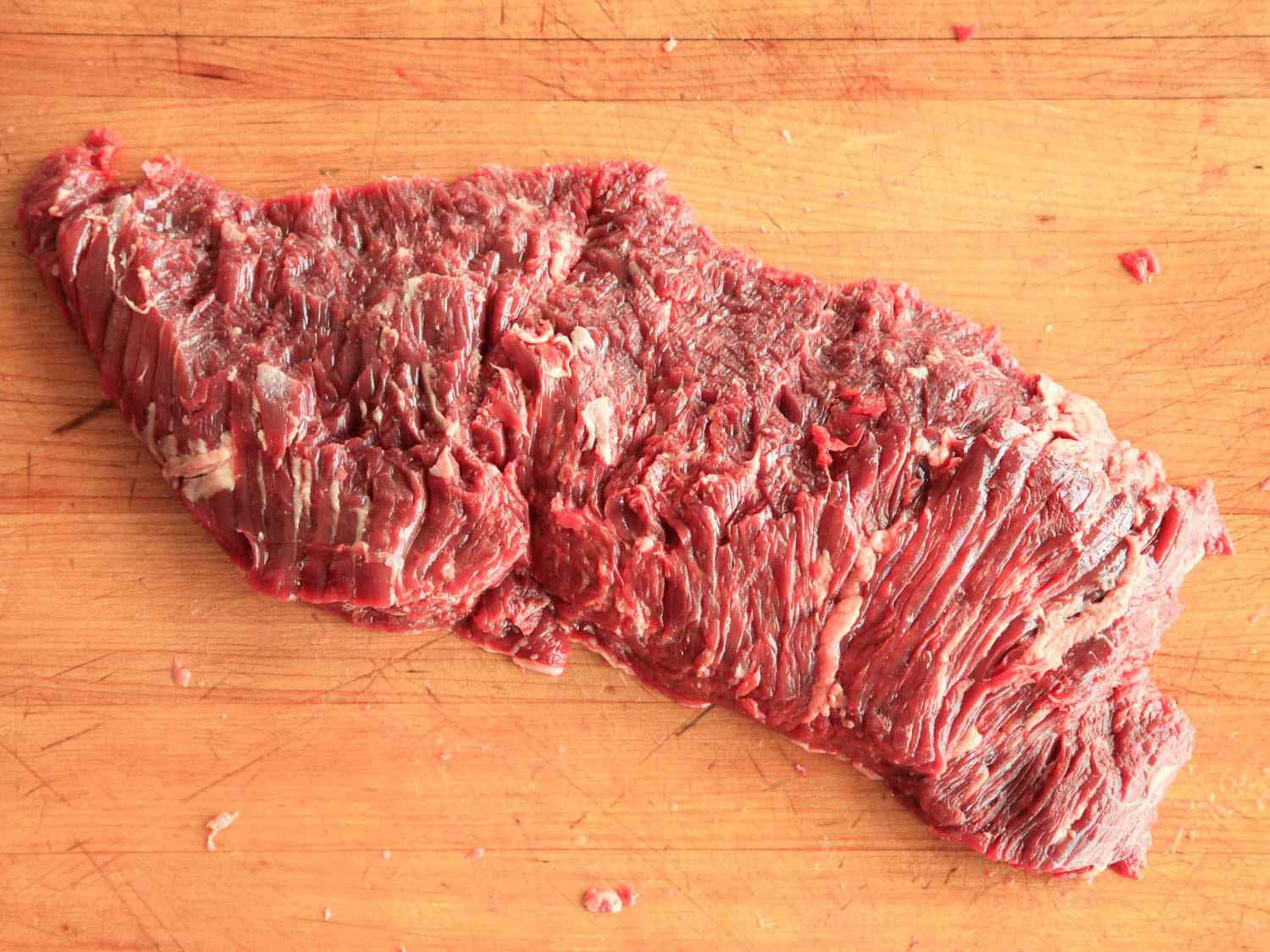 Inexpensive cut of flap steak on a wooden cutting board.
