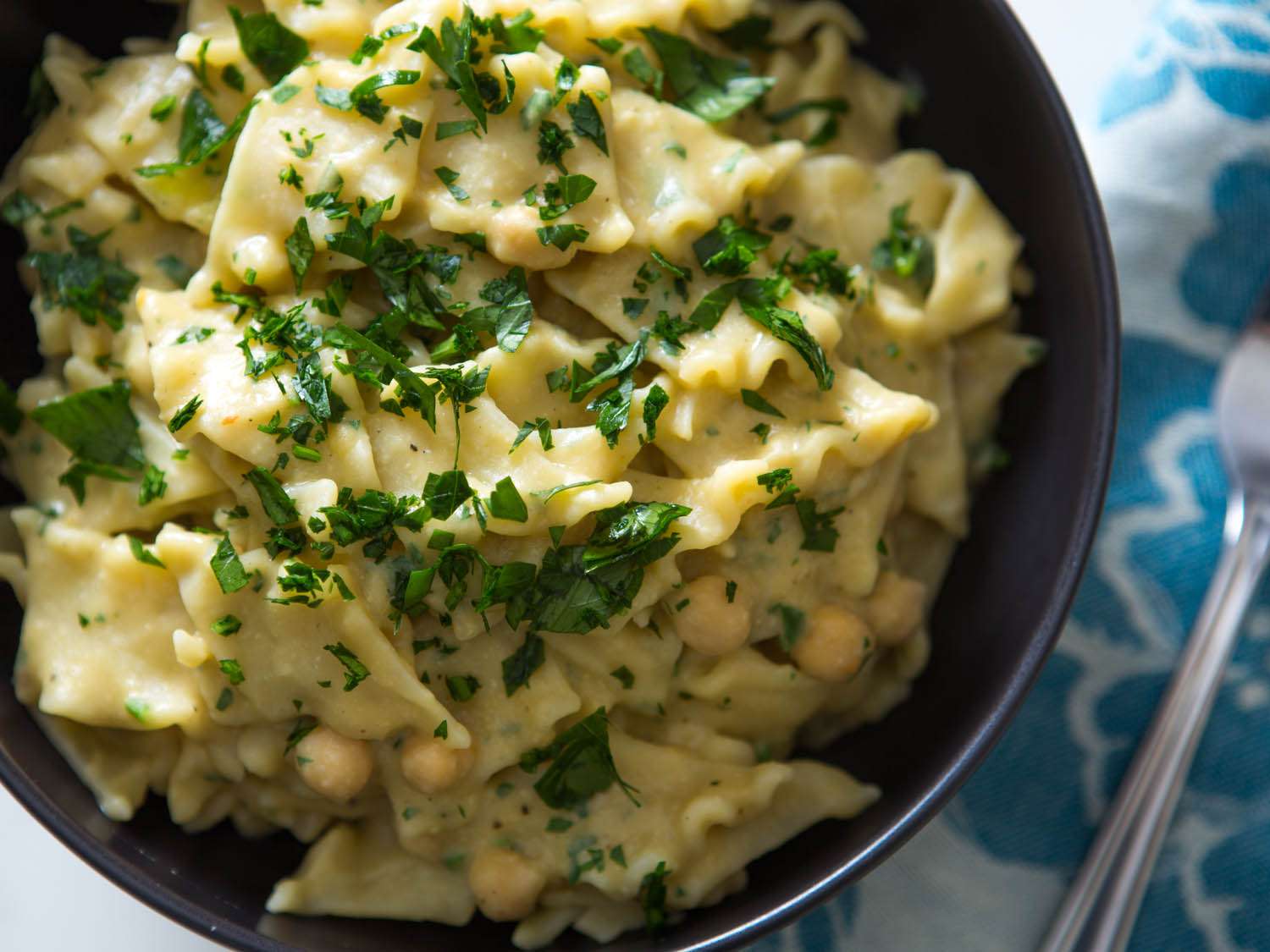 An overhead close-up of the finished vegan chickpea pasta, served in a dark bowl and showered with chopped parsley.