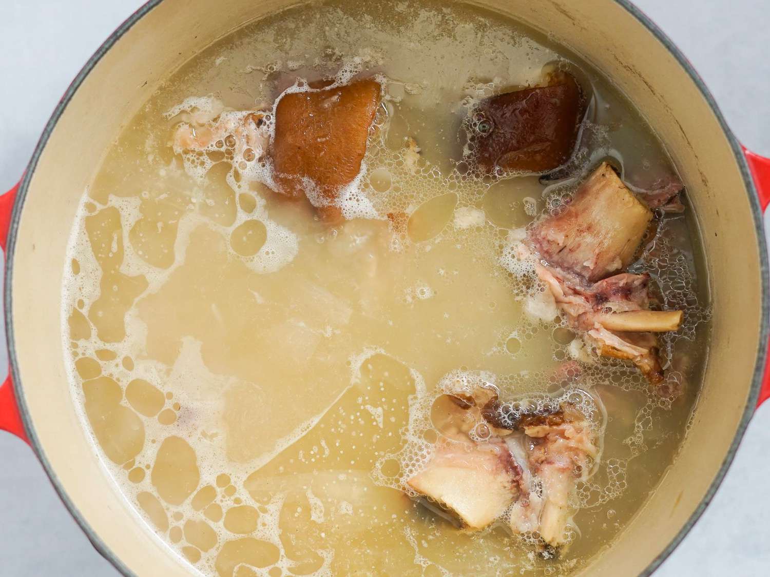 Ham hocks cooking in water mixture in a Dutch oven.