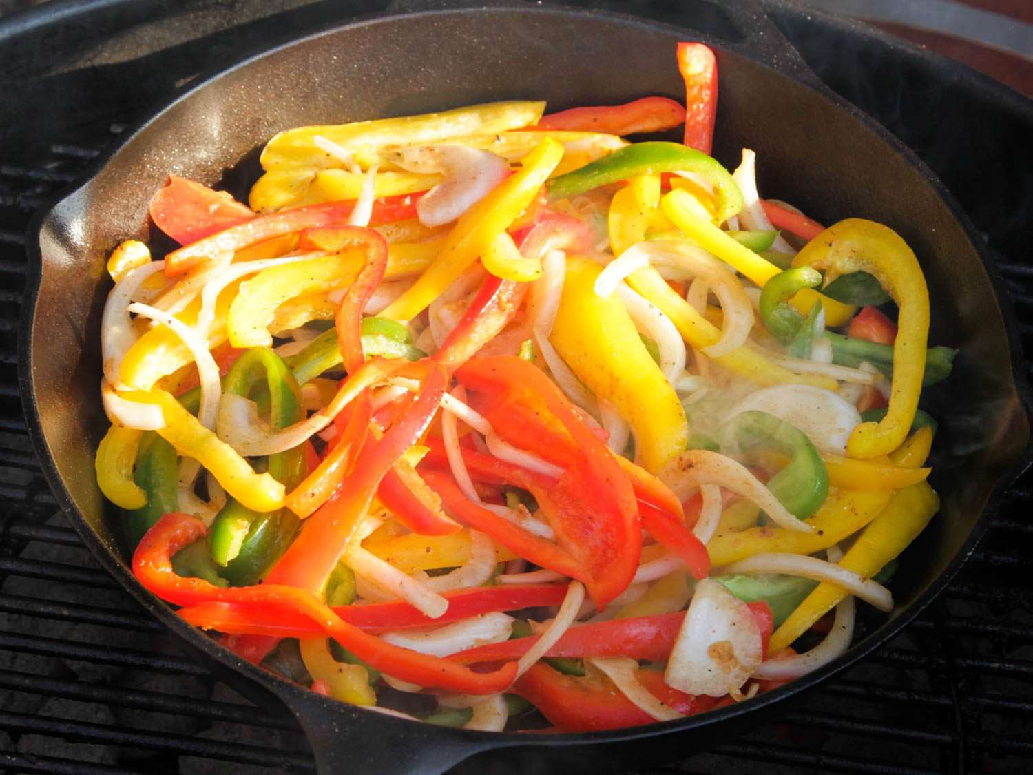 Onions and peppers cooking in a cast iron skillet on a grill for fajitas.