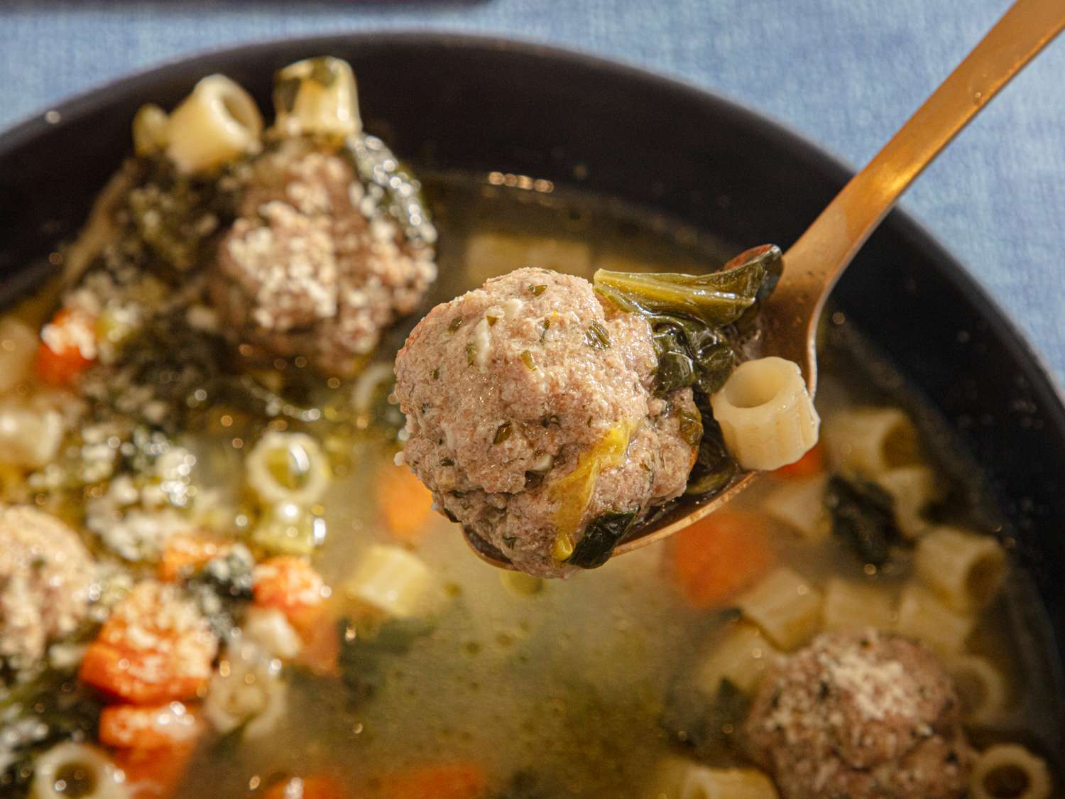 A spoon holding a meatball and pasta over a bowl of Italian wedding soup featuring vegetables and broth