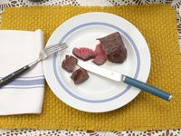 the material steak knife resting on a plate with cut up steak