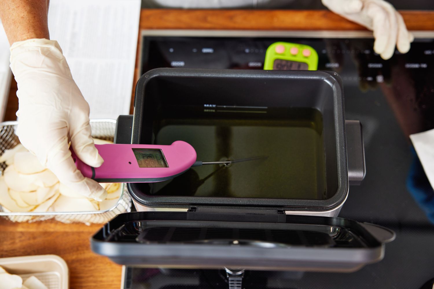 Hand using a thermometer to take the temperature of oil in a deep fryer