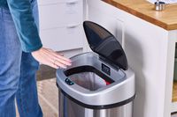 A person waves their hand over the iTouchless 13-Gallon Oval Stainless Steel Sensor Trash Can sensor