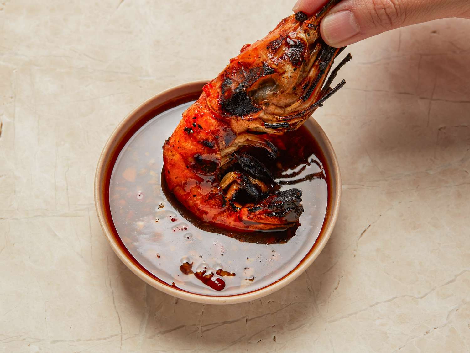 Grilled prawn being dipped into a bowl of sauce