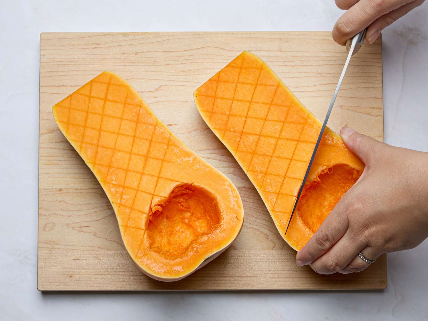 Halved butternut squash being scored and scooped on a wooden board