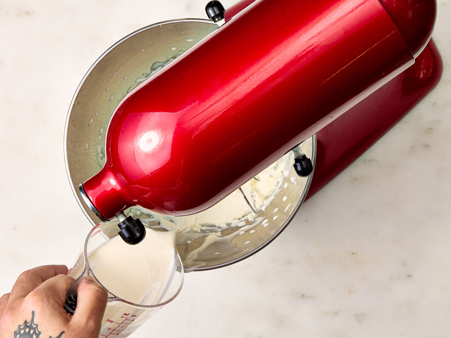 A person pouring liquid into a red stand mixer on a countertop