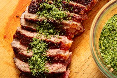 Sliced beef steak topped with herb seasoning served on a wooden cutting board
