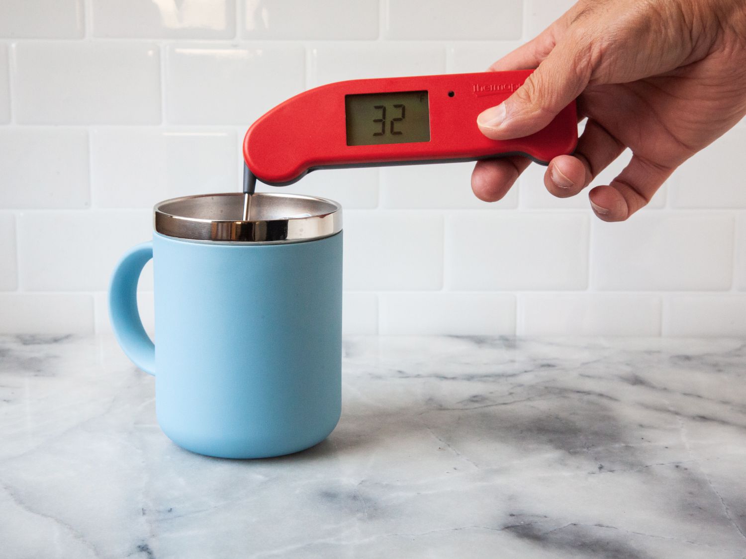Hand using ThermoWorks Thermapen ONE to check the temperature of liquid in a blue mug