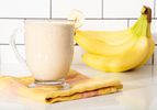 Banana smoothie in a glass cup with bananas in the background.